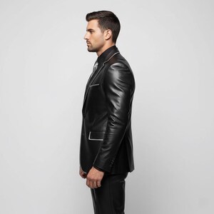 May include: A black leather suit with white trim, including a blazer and matching pants. The blazer features a notched lapel and a single-button closure. The suit is worn with a black shirt and a patterned tie.