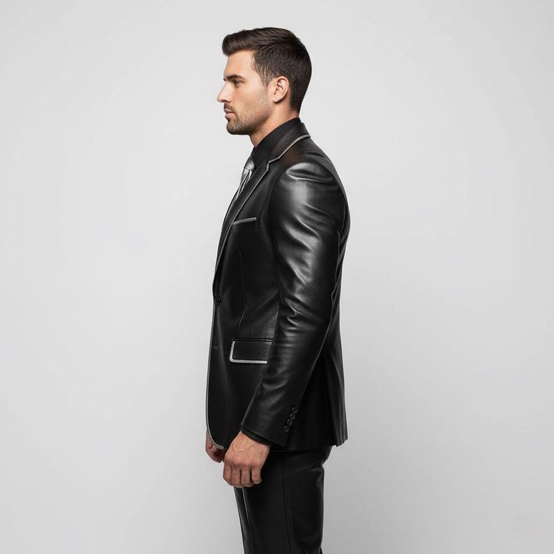 May include: A black leather suit with white trim, including a blazer and matching pants. The blazer features a notched lapel and a single-button closure. The suit is worn with a black shirt and a patterned tie.
