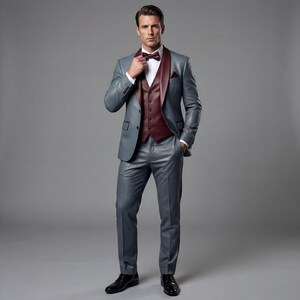May include: A three-piece gray suit with a burgundy vest and bow tie. The suit features a notched lapel and a pocket square. The man is wearing a white dress shirt and black dress shoes. The suit is a formal wear ensemble.