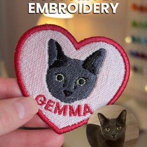 May include: Embroidered heart-shaped patch featuring a gray cat face with green eyes and the name "GEMMA" in red. The patch is outlined in red and has the text "CUSTOM PET EMBROIDERY" at the top. A small photo of the cat is in the lower right.
