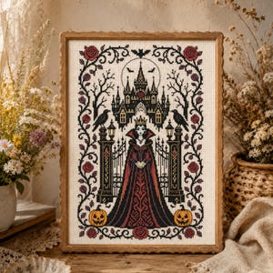 Può includere: Un ricamo a punto croce incorniciato raffigurante una figura centrale con un lungo abito scuro e una corona, davanti a un cancello di un castello gotico. Il disegno include corvi neri, zucche arancioni e un bordo di rose rosse su tessuto crema.