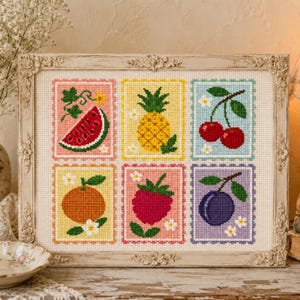 Könnte beinhalten: Ein Kreuzstich-Stickbild in einem dekorativen cremefarbenen Rahmen mit sechs rechteckigen Fruchtmotiven: ein Wassermelonenstück, eine Ananas, zwei Kirschen, eine Orange, eine Himbeere und eine Pflaume, jeweils mit kleinen weißen Blüten.