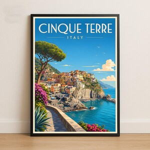 May include: A framed travel poster featuring the text CINQUE TERRE ITALY. The illustration depicts a coastal village with colourful buildings on a cliffside, a blue sea, a stone path with pink flowers, a large pine tree, and a clear blue sky.