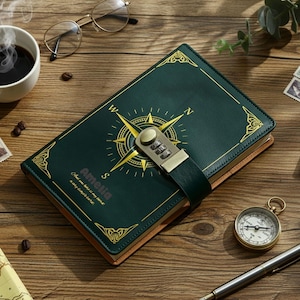 May include: A green leather journal with a compass design and a combination lock. The journal has gold accents and the name "Amelia" printed on the cover. A cup of coffee, glasses, and a compass are on the wooden surface.
