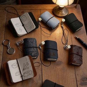 May include: Several small leather notebooks in shades of blue, brown, and black, each with a lanyard. Some have embossed patterns or initials. Open notebooks show simple drawings of weather and travel. Measurements are not available.