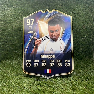 Puede incluir: Una tarjeta coleccionable rectangular que muestra al futbolista Mbappé con una camiseta blanca. La tarjeta presenta una valoración general de 97, posición ST y estadísticas: 99 PAC, 97 SHO, 87 PAS, 97 DRI, 55 DEF y 83 PHY. Una pequeña bandera francesa aparece impresa en la parte inferior.
