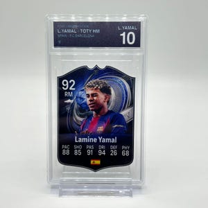 Puede incluir: Una tarjeta coleccionable de fútbol de Lamine Yamal, calificada y encapsulada en un soporte de plástico transparente. La tarjeta presenta una foto del jugador con la camiseta del Barcelona, con estadísticas y el número 10. La tarjeta está etiquetada como "TOTY HM" y "FC Barcelona".