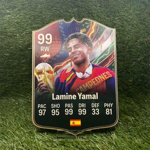 May include: A rectangular sports trading card featuring a portrait of Lamine Yamal holding a gold trophy. The card displays the text 99 RW, the name Lamine Yamal, and statistics including PAC 97, SHO 95, PAS 99, DRI 99, DEF 33, PHY 81, with a small Spanish flag.