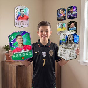 Peut inclure: Grandes cartes décoratives de joueurs de football représentant Cristiano Ronaldo, Ronaldinho, Gareth Bale, Lamine Yamal, Lionel Messi et Erling Haaland. Les cartes affichent des statistiques, des noms et des drapeaux. La carte Ronaldo est verte, les autres sont blanches ou noires.
