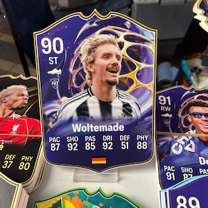 Puede incluir: Tarjetas coleccionables de fútbol con retratos de jugadores y estadísticas. La tarjeta principal muestra a Woltemade, con una calificación de 90, con una bandera alemana. Se ven otras tarjetas.