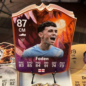May include: A collectible card featuring a player named Foden. The card has a vibrant design with a portrait of the player and various statistics. The card is 87 cm tall and has a soccer theme.