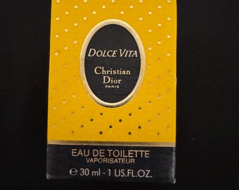 Könnte beinhalten: Eine gelb-schwarze Dolce Vita Christian Dior Parfümbox. Die Box hat ein goldenes Oval mit den Worten "DOLCE VITA" und "Christian Dior PARIS". Auf der Unterseite der Box steht "EAU DE TOILETTE VAPORISATEUR e 30 ml - 1 US.FL.OZ."