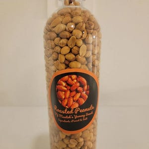 May include: A clear plastic bottle filled with roasted peanuts. The label features a circular image of reddish-brown peanuts and the text: Roasted Peanuts, Try Mantoh's Yummy Snack, Ingredients: Peanut & Salt. The bottle is packed with light brown peanuts.
