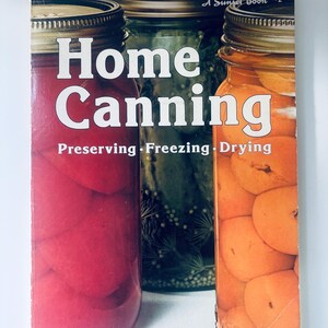May include: A softcover book titled Home Canning Preserving Freezing Drying by A Sunset Book. The cover features three glass jars filled with red, green, and orange preserved produce, each topped with a metallic screw-top lid against a white background.