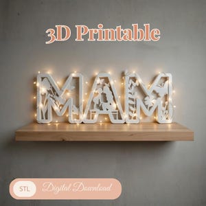 Könnte beinhalten: Weißes, 3D-druckbares Schild mit der Aufschrift "MAM" mit floralen und Schmetterlingsausschnitten, beleuchtet von Lichterketten. Das Schild wird auf einem Holzregal präsentiert. Der Text oben lautet "3D Printable", und darunter "Digital Download".