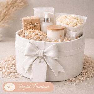 Peut inclure: Un coffret cadeau blanc orné d'un grand nœud et d'une étiquette vierge. Il contient divers articles, dont un petit cadeau emballé, une bouteille de lotion, une bougie et un bouquet de fleurs blanches. Le coffret est rempli de garnitures décoratives.