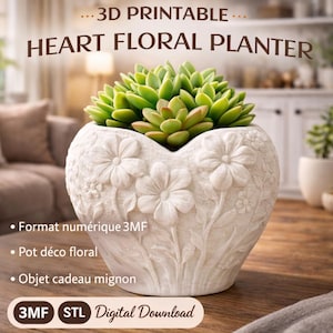 Puede incluir: Una maceta floral blanca en forma de corazón con detalles de flores en relieve, que contiene una planta suculenta verde. La maceta tiene el texto "...3D PRINTABLE... HEART FLORAL PLANTER" y "3MF STL Digital Download".