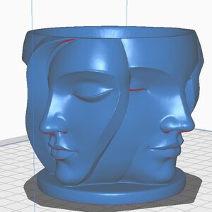 May include: A blue decorative planter featuring three sculpted faces. The faces are in profile, with one face showing closed eyes. The planter has a round base and a wide opening at the top.