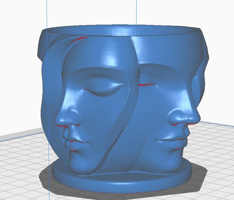 May include: A blue decorative planter featuring three sculpted faces. The faces are in profile, with one face showing closed eyes. The planter has a round base and a wide opening at the top.