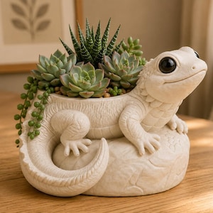 Può includere: Una fioriera a forma di lucertola in ceramica bianca piena di piante grasse. La lucertola è scolpita con squame dettagliate e presenta grandi occhi scuri. La fioriera contiene una varietà di piante grasse verdi.
