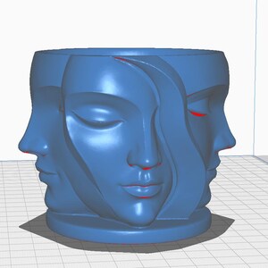 May include: A blue cylindrical planter featuring the sculpted faces of three women. The faces are in profile and have closed eyes and serene expressions. The planter is a solid blue color and sits on a small base.