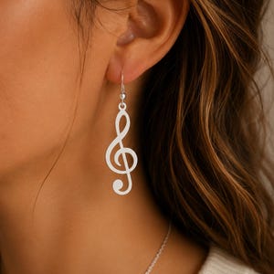May include: Silver-colored treble clef earrings. The earrings are a simple, elegant design, with a hook at the top for the ear. The treble clef is a musical symbol, and these earrings would be a great gift for a musician or music lover.