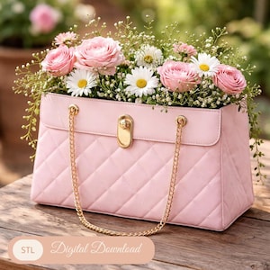 Puede incluir: Una jardinera en forma de bolso rosa acolchado, llena de rosas rosas, margaritas blancas y vegetación. El bolso tiene correas de cadena doradas y un cierre dorado. La jardinera está sobre una superficie de madera, con un fondo borroso de flores.