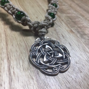 Op de afbeelding: Een zilveren Keltische knoop hanger ketting met een bruin hennepkoord en groene glazen kralen.