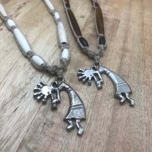 May include: Two necklaces with silver pendants depicting a stylized Native American dancer. One necklace has white beads and the other has brown beads.