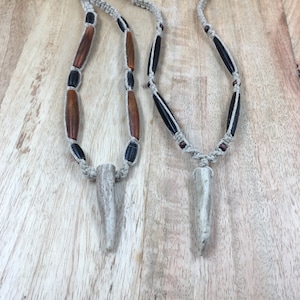 May include: Two necklaces with brown and black beads and a bone pendant. The necklaces are made with a natural fiber cord.
