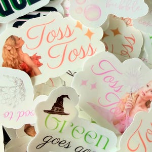 May include: A collection of white cloud-shaped stickers with various designs and text. Some stickers feature illustrations of a woman, a witch's hat, and bubbles. Text includes "Toss Toss" and "Green goes good".
