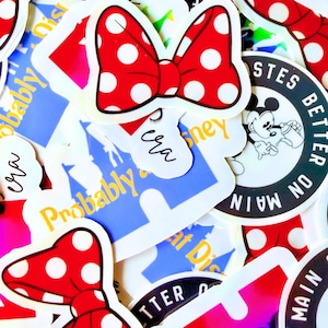 May include: A collection of colorful stickers featuring a red bow with white polka dots, and other Disney-themed designs. Some stickers have text that reads "Probably", "Tastes Better on Main", and "In my era".