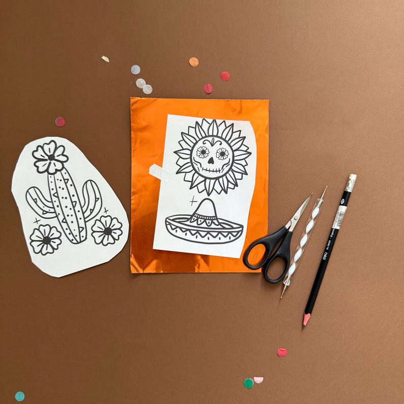 May include: A still-life composition featuring Dia de los Muertos-themed art supplies. Includes a cactus and a sun with a skull design, a sombrero, scissors, a pencil, and other tools. The items are arranged on a brown surface with orange foil.