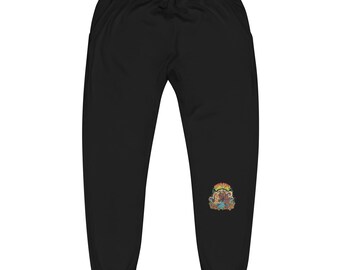 Può includere: Pantaloni della tuta neri con vita con coulisse. Una grafica colorata è presente sulla gamba inferiore destra. La grafica presenta testo e un'illustrazione di un orso e altri elementi.