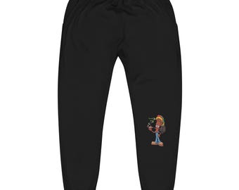 Può includere: Pantaloni della tuta neri con vita con coulisse e grafica a cartoni animati di una persona che fuma una sigaretta. La grafica presenta una persona con dreadlocks, un cappello rosso, giallo e verde e jeans blu. I pantaloni della tuta sono in materiale morbido.