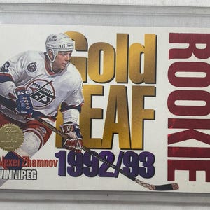 May include: A Gold Leaf 1992/93 hockey card featuring Alexi Zhamnov of the Winnipeg Jets. The card has a gold foil background with the word "Gold Leaf" in large gold letters and "Rookie" in red.