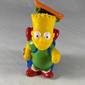 May include: A yellow Bart Simpson figurine with a skateboard on his head and a backpack. Bart wears a green shirt, red shoes, and blue shorts. The skateboard is orange and green. The figurine is a collectible item.