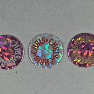 May include: Five circular stickers with a holographic, shattered-glass effect. Each sticker features the word CHRIS repeated in a circular pattern around the edge. The stickers display varying color shifts, including red, purple, and silver tones.