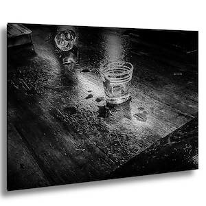 Può includere: Fotografia in bianco e nero di un tavolo di legno con due bicchierini vuoti. Un bicchierino è in posizione verticale, l'altro è rovesciato. Gocce e schizzi d'acqua sono visibili sulla superficie del tavolo, riflettendo la luce.