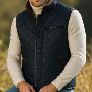 May include: A navy blue quilted vest with brown trim and a brown fur-lined collar. The vest has a zipper pocket on the chest and is buttoned down the front. The person is wearing a cream-colored turtleneck sweater underneath.