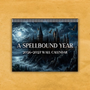 May include: A wall calendar with a fantasy castle illustration under a moonlit sky. The calendar is titled "A Spellbound Year" and covers the years 2026-2027. The calendar has a spiral binding at the top and is set against a tan background.
