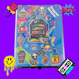 Puede incluir: Un cuaderno azul Trapper Keeper cubierto de coloridas pegatinas con temática de los años 90. Las pegatinas incluyen un zombi, un perro esqueleto, un oso de peluche, un helado y el texto "Emotional Support Kindle".