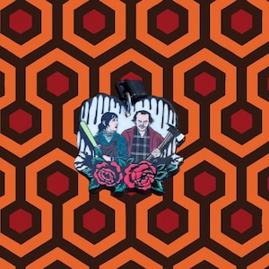 May include: A heart-shaped enamel pin featuring a scene from a movie. The pin depicts a man and a woman, with red roses at the bottom. The background is a repeating pattern of orange and brown hexagons.