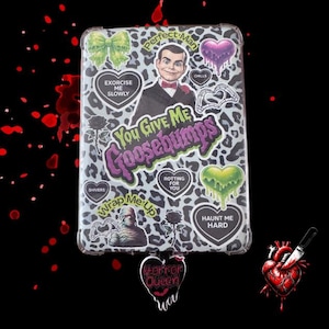 May include: A clear phone case with a leopard print design, featuring stickers with horror-themed graphics and text. The stickers include a ventriloquist dummy, hearts, and the phrase "You Give Me Goosebumps."