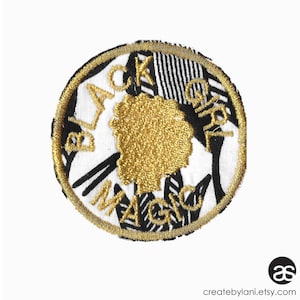 May include: A round, gold embroidered patch with the words "Black Girl Magic" in a black and white patterned background.