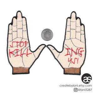 Peut inclure: Deux patchs brodés avec des mains tendues, chacun avec un message différent. La main gauche dit "STOP KILLING" en lettres rouges. La main droite dit "ING YOU" en lettres rouges.