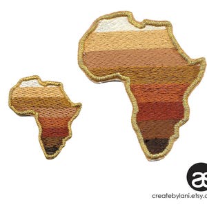 May include: Two embroidered patches in the shape of the continent of Africa. The larger patch is brown, tan, and white, while the smaller patch is brown, tan, and orange. Both patches have a gold outline.