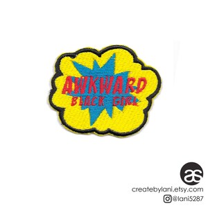 May include: Yellow embroidered patch with a black outline in the shape of a speech bubble. The speech bubble has a blue starburst inside and the text "AWKWARD BLACK GIRL" in red.