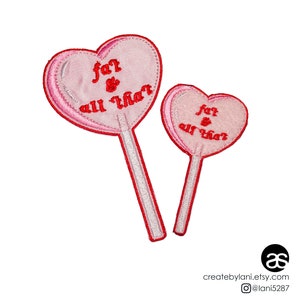 May include: Two pink heart-shaped lollipop patches with red embroidery that reads "for & all that".