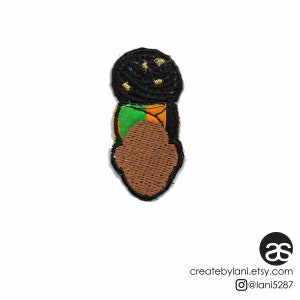 May include: An embroidered iron-on patch featuring a black woman with a green, orange, and black head wrap and gold accents. The patch is approximately 2 inches in diameter.